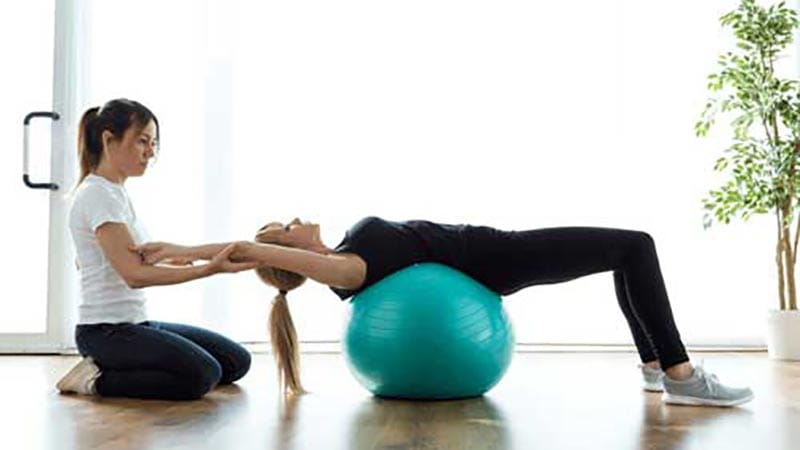 Physiotherapist assisting woman on fitness ball