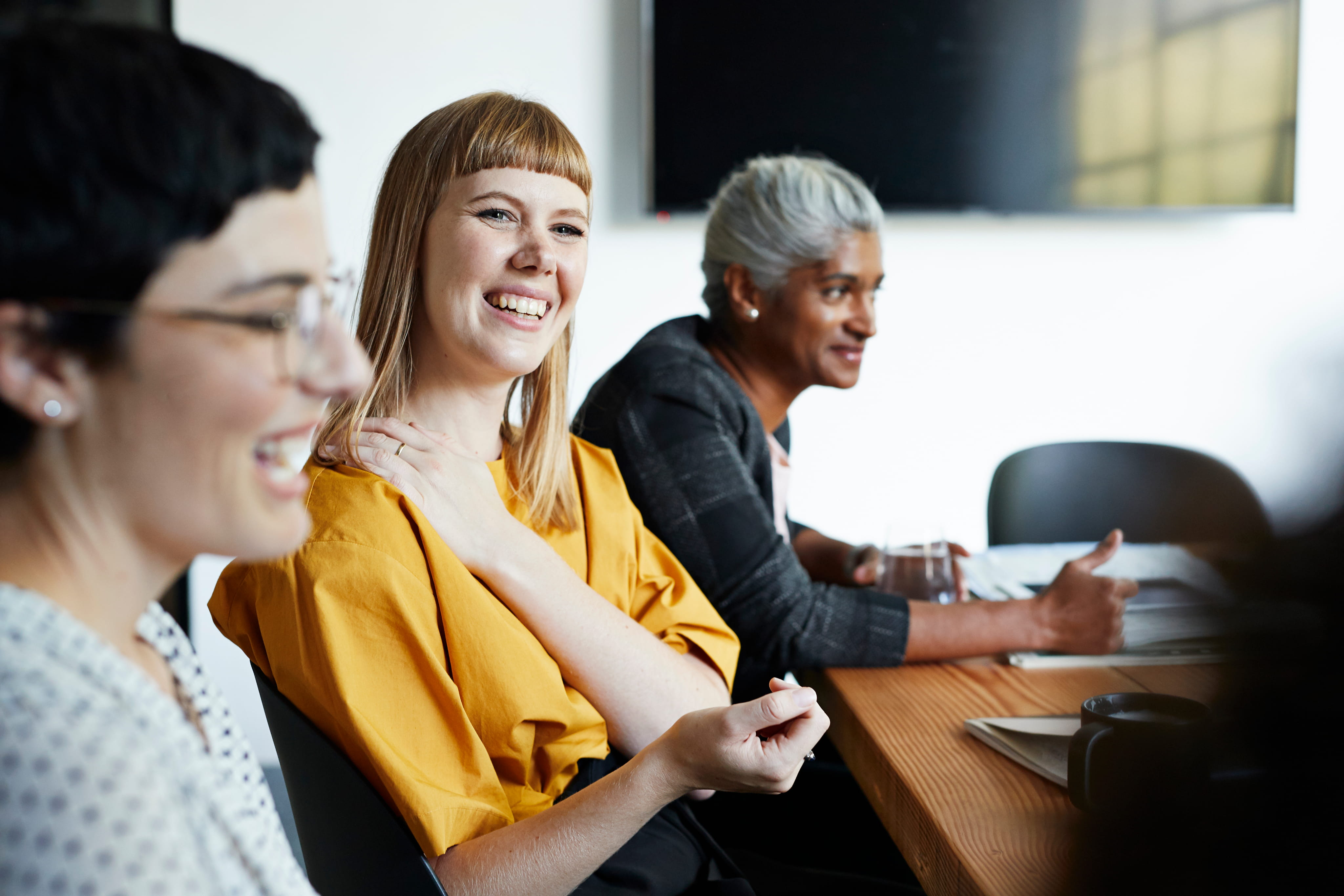 Three women laughing while sitting around a board table