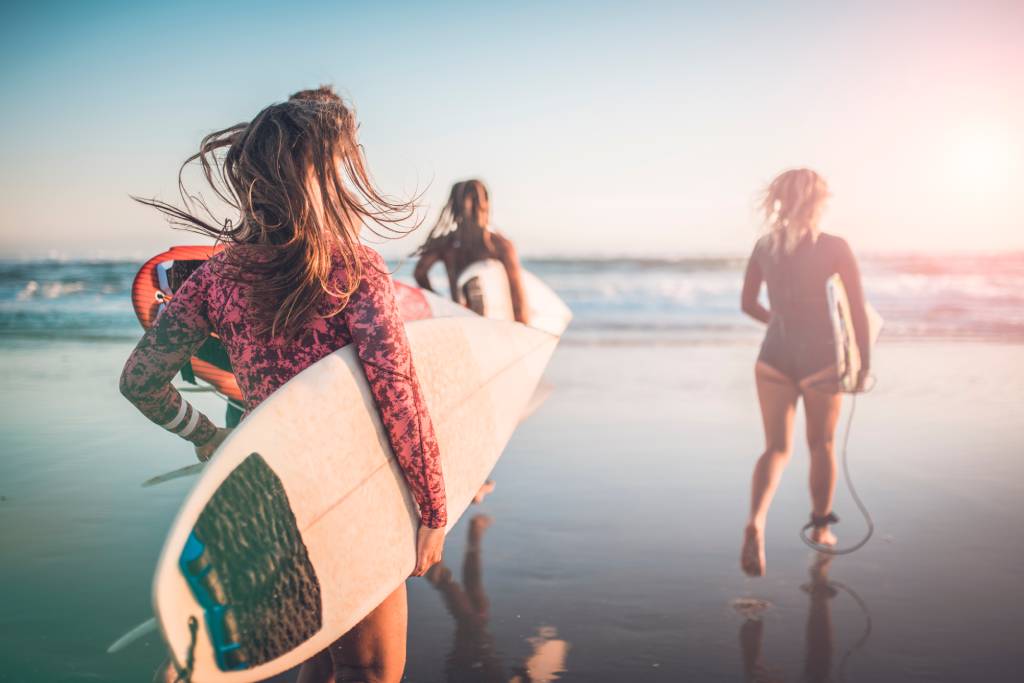 Three women running towards the ocean with surfboards