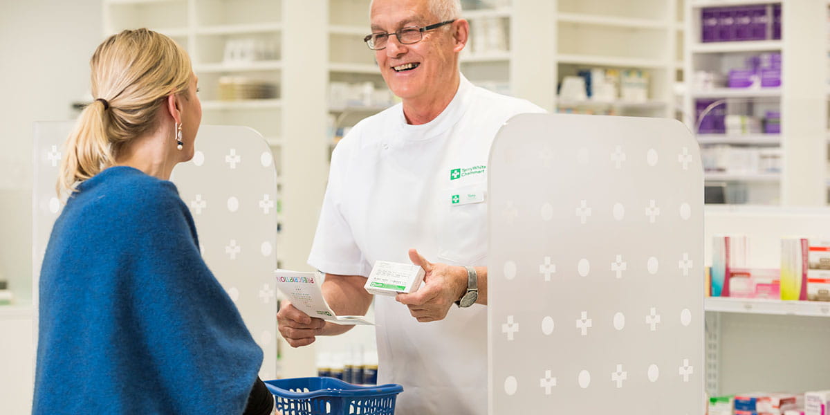 Male TerryWhite pharmacist hands prescription to female customer
