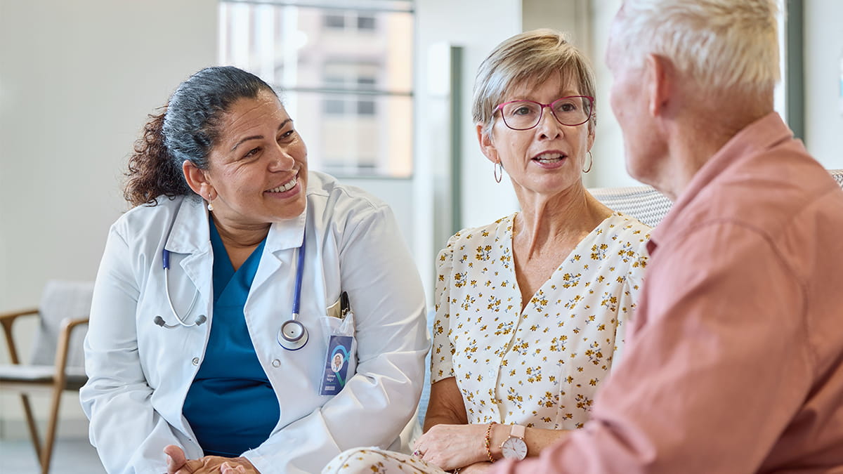 Healthcare professional speaking with two adults during a personalised health coaching consultation.