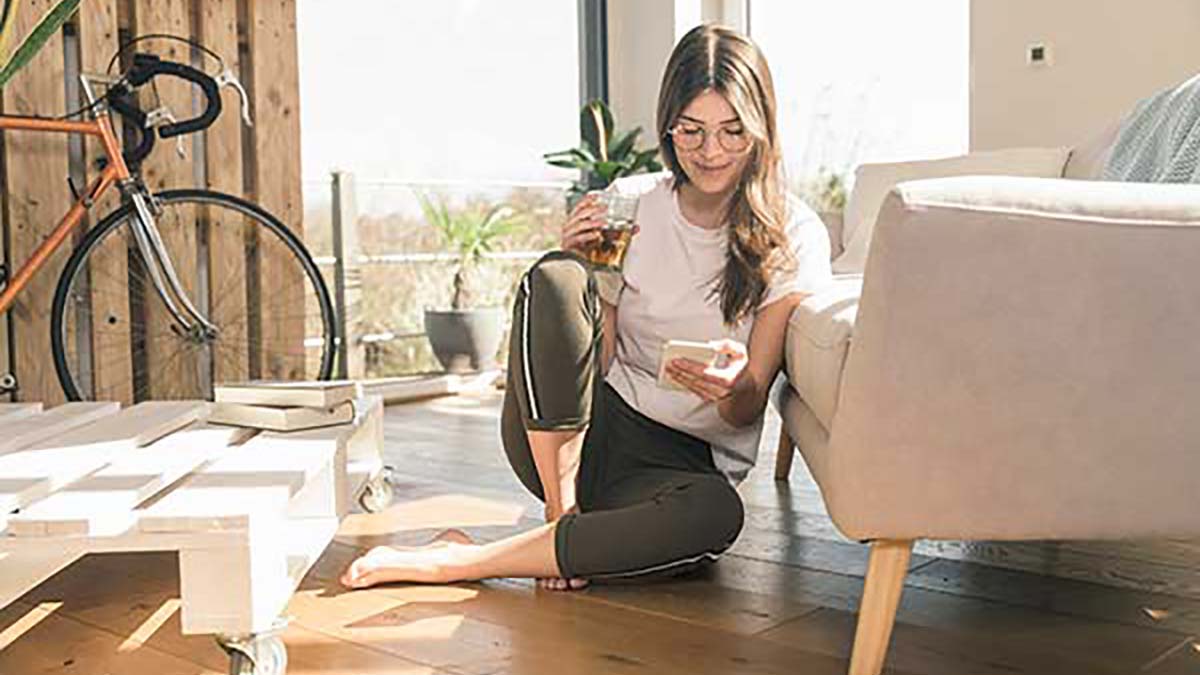 Woman sitting on the floor looking at her phone and drinking a cup of tea