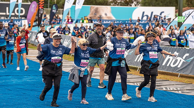 Team of four women holding hands as they run across the finish line