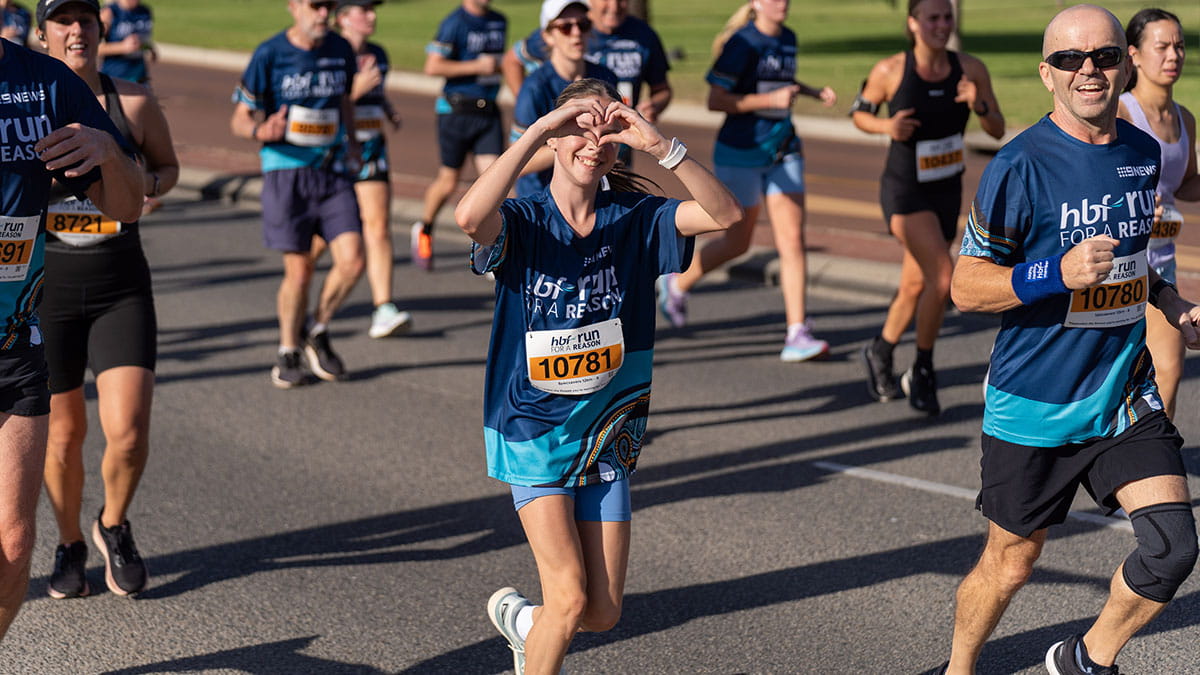 HBF Run for a Reason participant making heart gesture as she crosses finish line