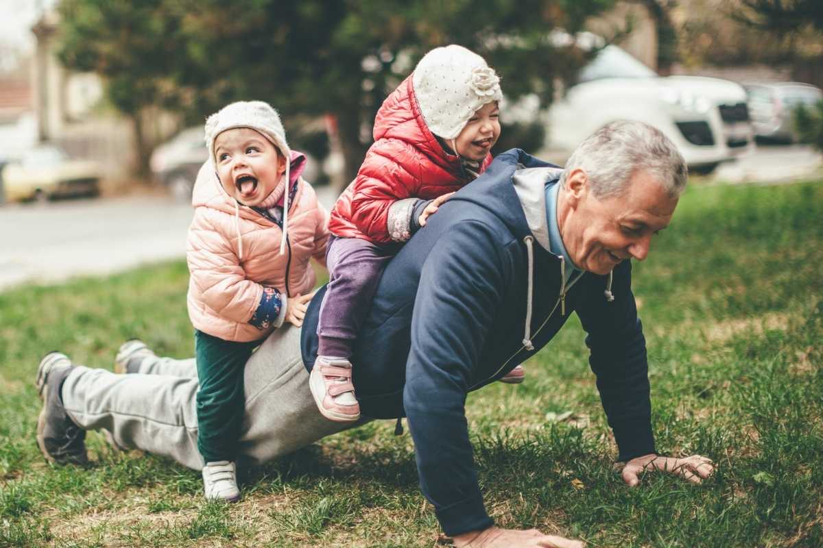 A grandfather doing a push-up with two cute children climbing on his back