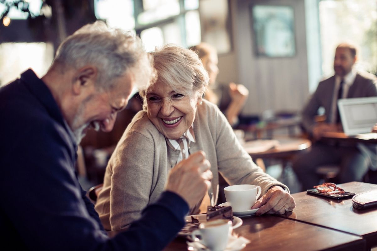 A senior man and woman laughing together in a cafe