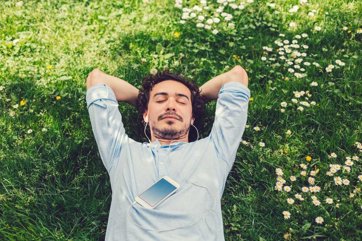 A young man lying on the grass relaxing and listening to music