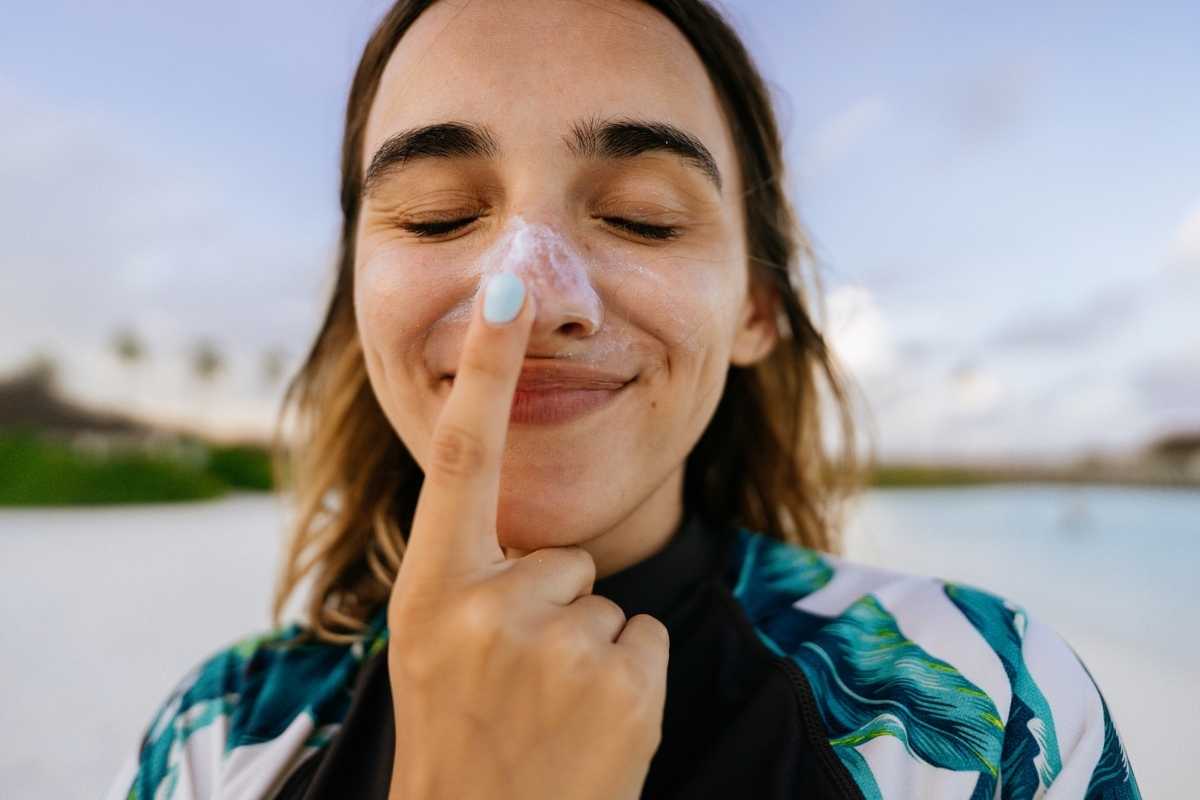 A young woman at the beach putting sunscreen on her nose and smiling