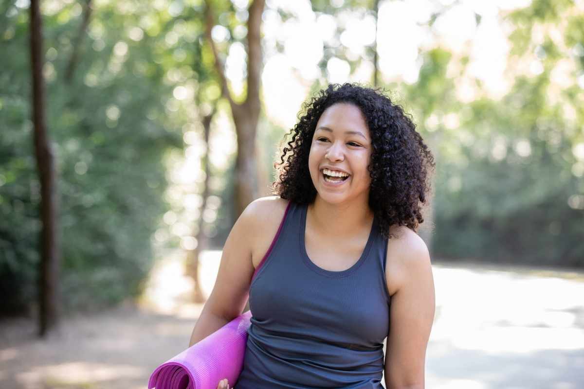 A happy woman outdoors with a yoga mat