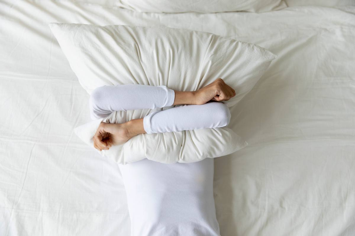 Woman covers face with pillow in dread