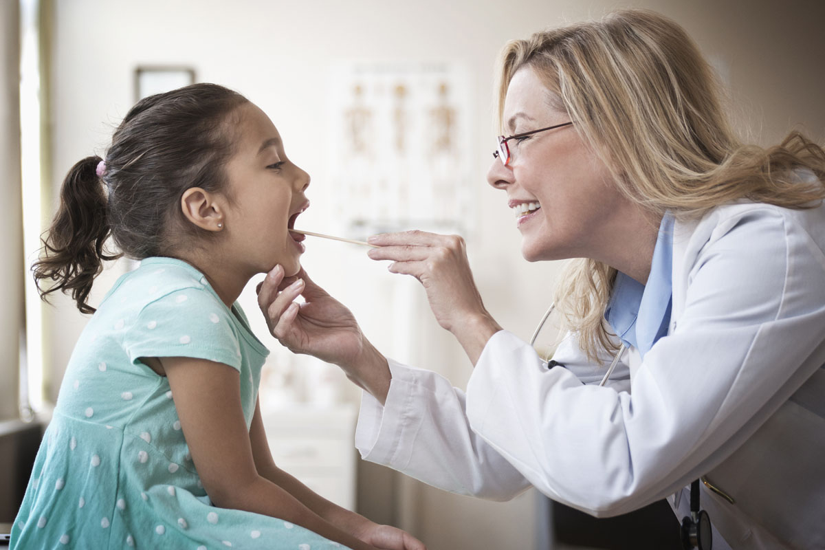 Female doctor inspecting young girls throat