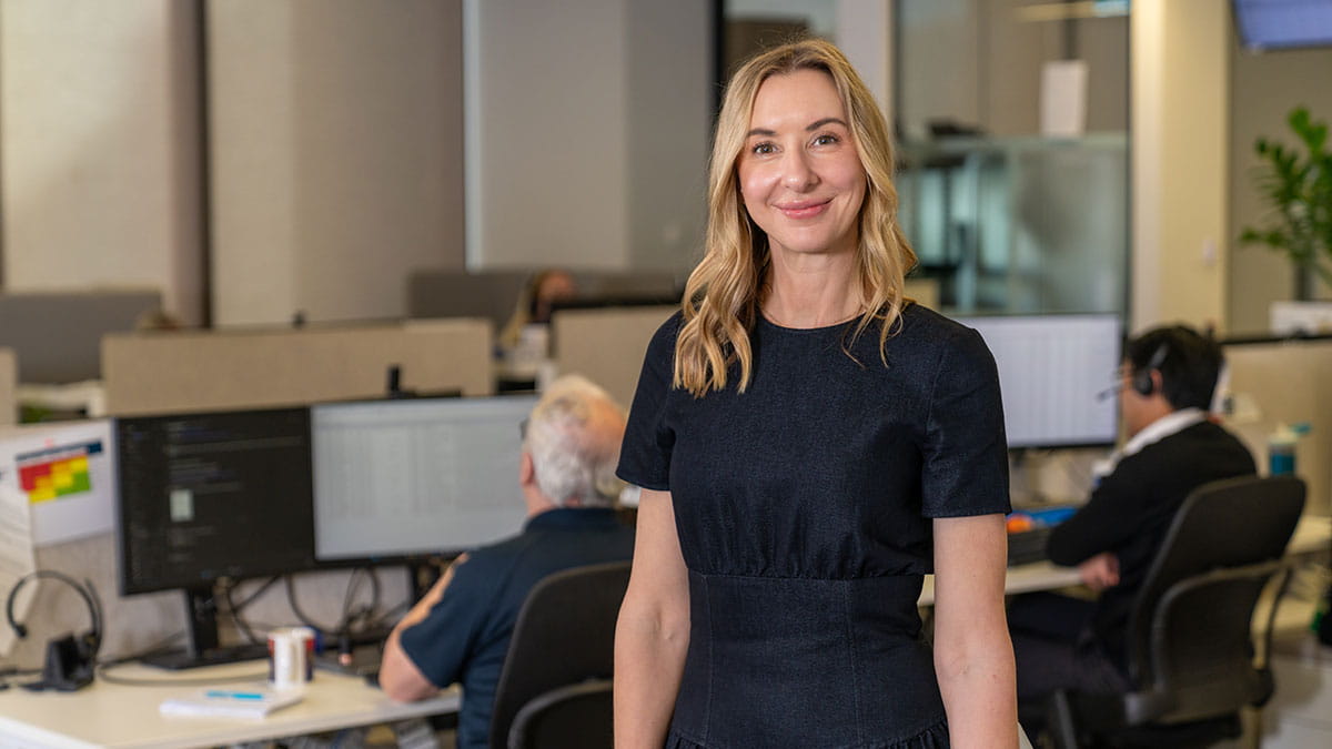 Employee standing in an office workspace with colleagues working in the background, illustrating flexible work and team support at HBF.